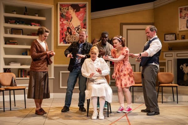 Doc.Doc5 Blanche, played by Joanna Hudson-Fox, sits anxiously in the doctor’s waiting room as other characters react around her in Doc Doc, highlighting her germophobia and compulsive behaviors.