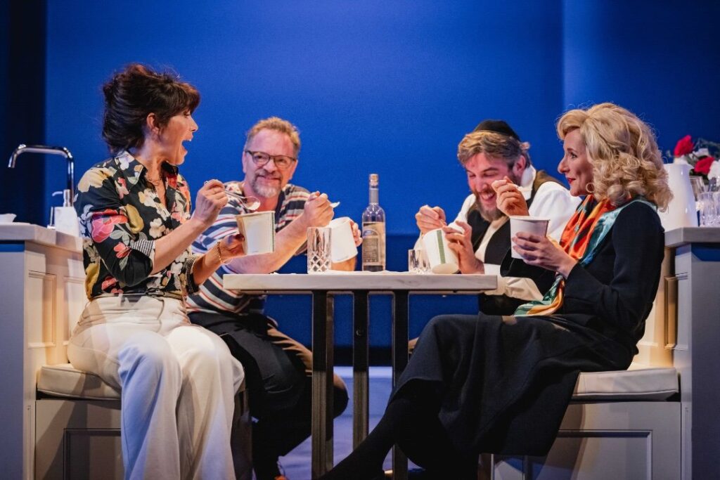 Caroline Catz, Joshua Malina, Simon Yadoo, and Dorothea Myer-Bennett sharing a light-hearted moment while eating takeout on stage,