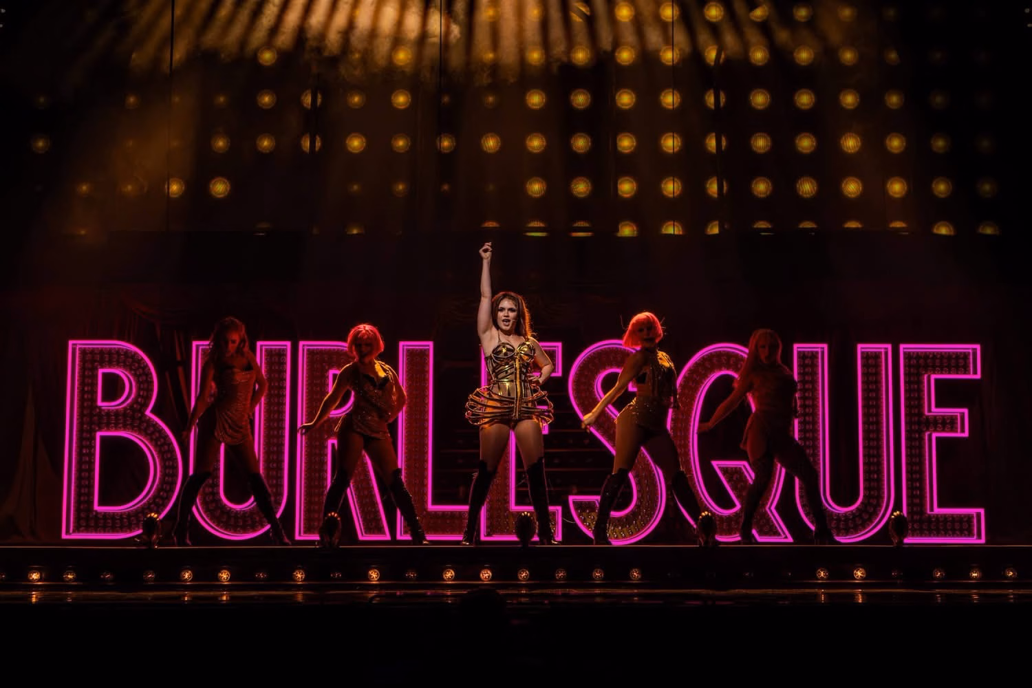 Burlesque The Musical UK Tour performer centre stage with dancers in front of a glowing pink Burlesque sign